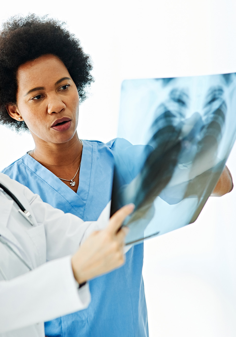 Radiologist examining x-ray An x-ray technician in blue scrubs is holding up an e-ray to examine the image and bones.