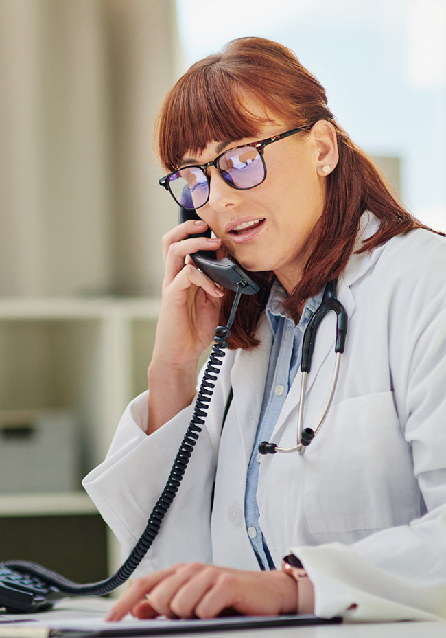 A healthcare professional in a hospital talks on the phone while pointing to a pad of paper.